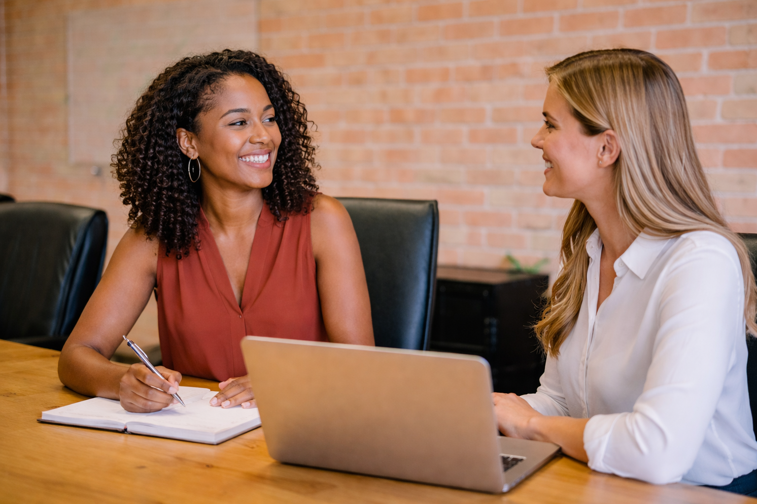 Two executives collaborating at a table with laptop and notebook